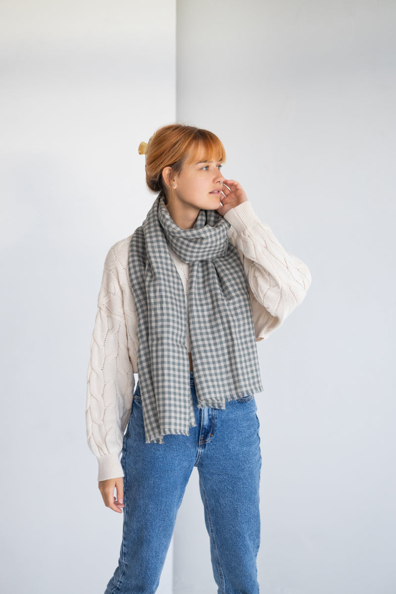 Woman wearing a checkered linen scarf, white shirt, and blue jeans against a plain background