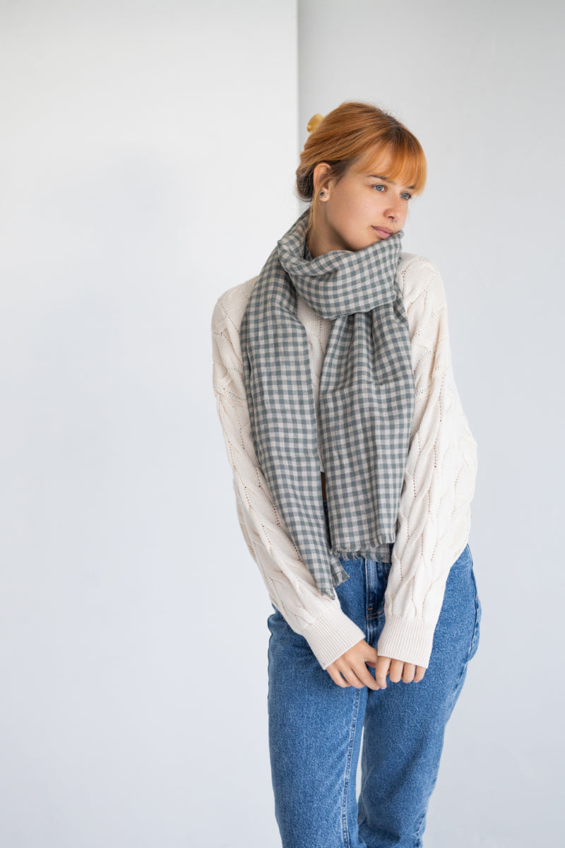Woman wearing a checkered len inscarf, white shirt, and blue jeans against a plain background