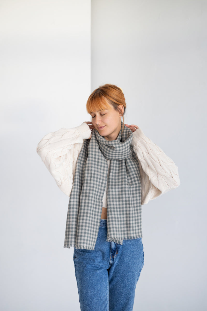 Woman wearing a plaid linen scarf and blue jeans against a white background