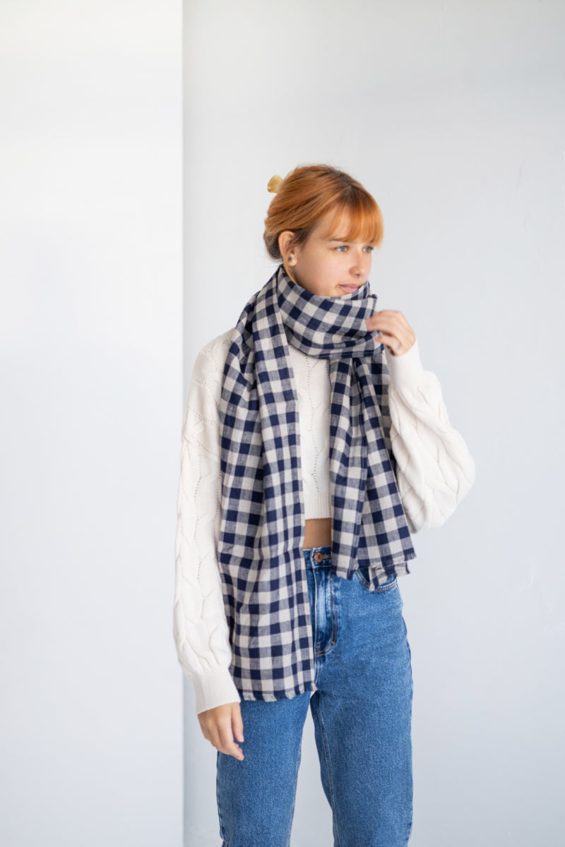 Person wearing a blue and white checkered linen scarf with a plain background