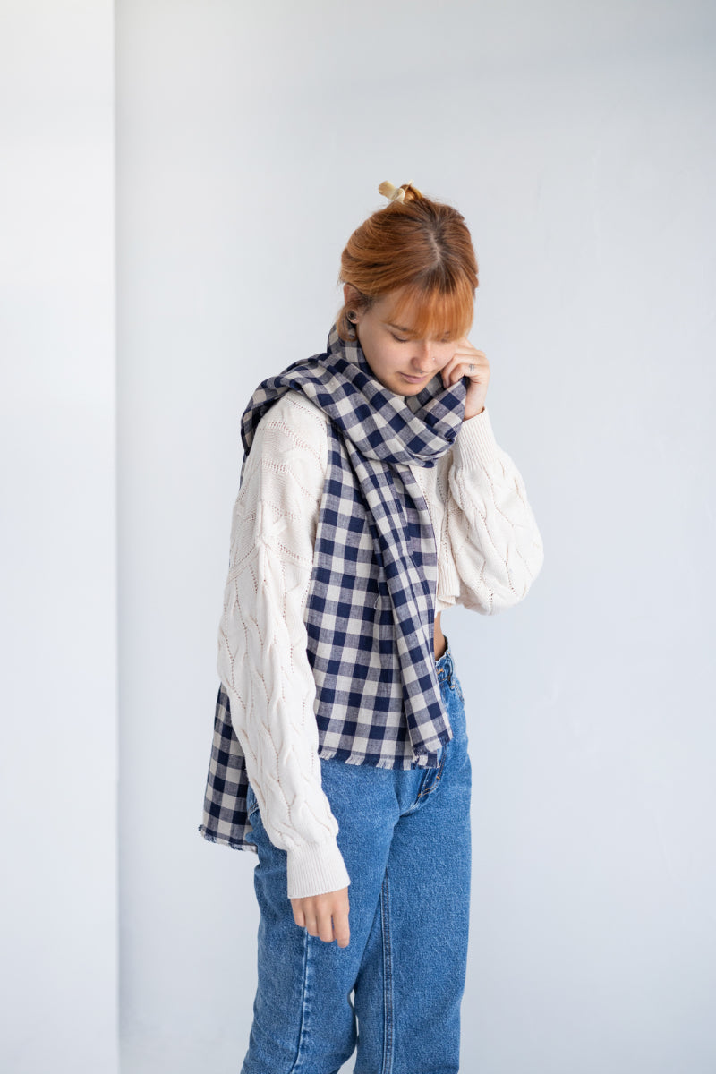 Person wearing a blue and white checkered linen scarf with a plain background
