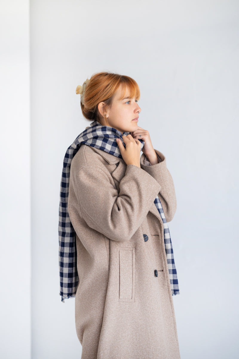 Woman wearing a beige linen coat with a plaid scarf against a white background