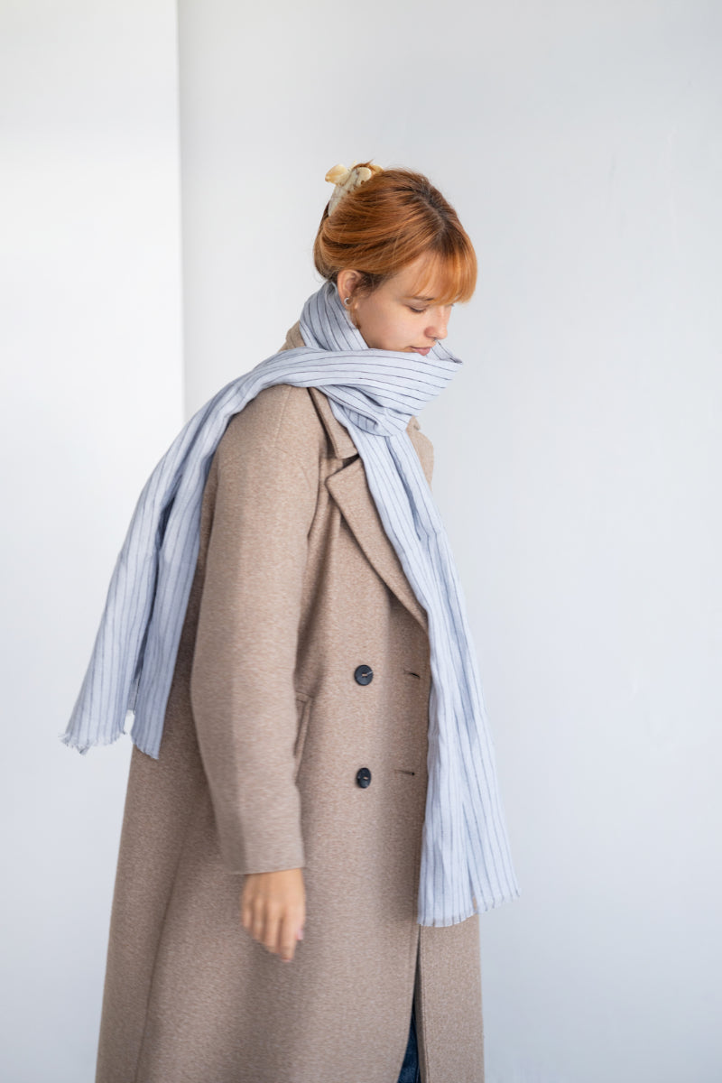 Person wearing a long coat and light gray linen scarf against a white background
