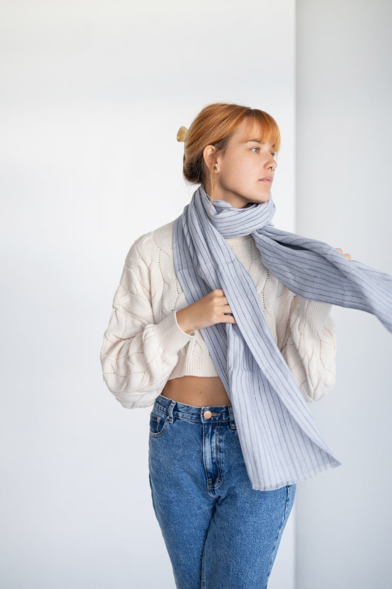 Person wearing a long coat and light gray linen scarf against a white background