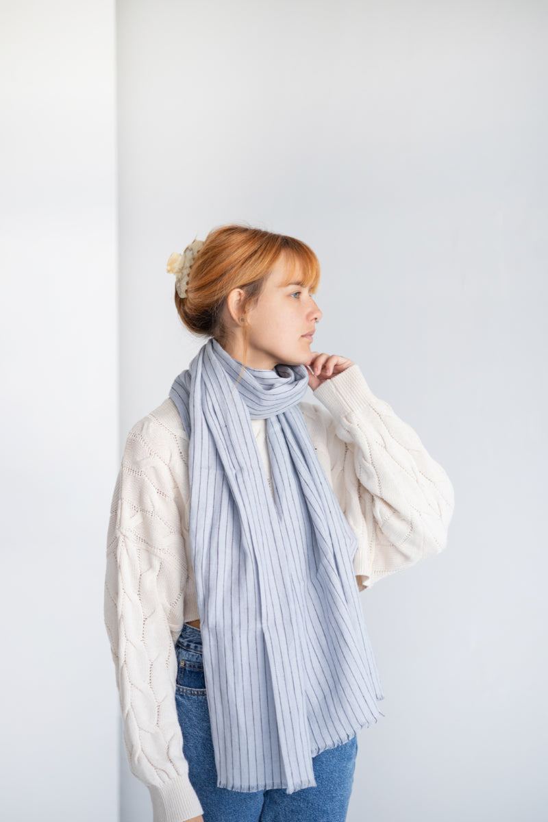 Person wearing a long coat and light gray linen scarf against a white background