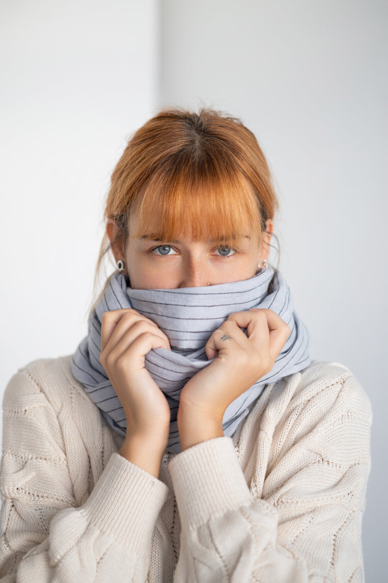 Woman wearing a striped linen scarf and white sweater against a plain background