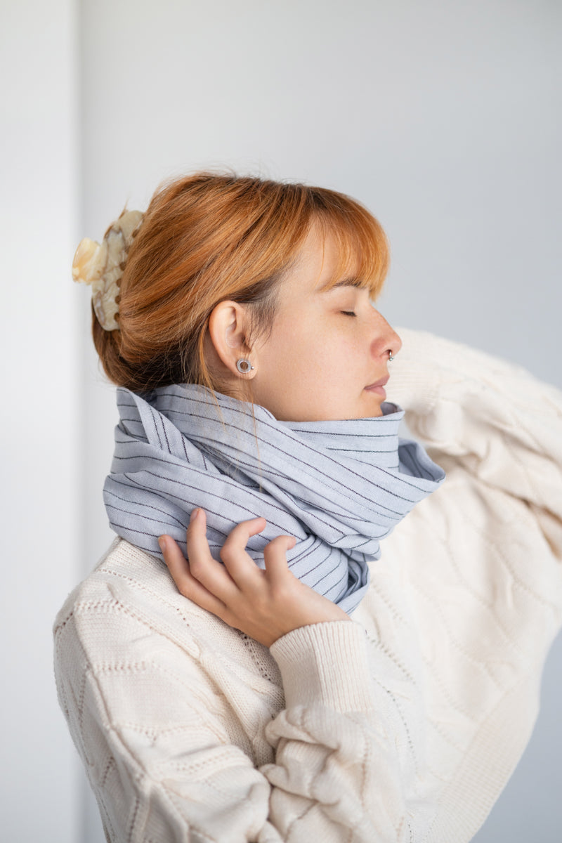 Woman wearing a striped linen scarf and white sweater against a plain background