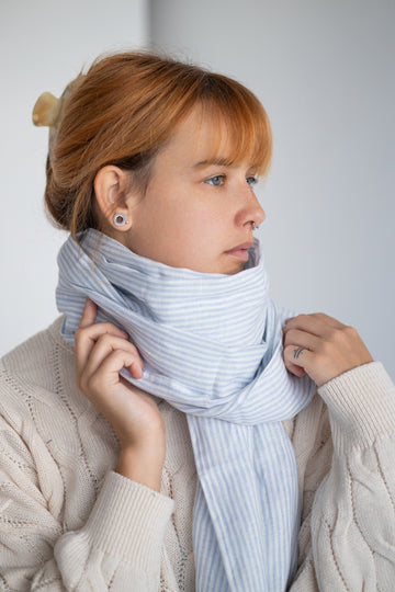 Woman wearing a striped linen scarf and white sweater against a plain background