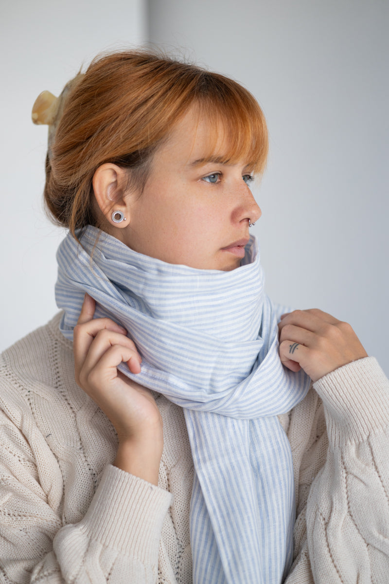 Woman wearing a striped linen scarf and white sweater against a plain background
