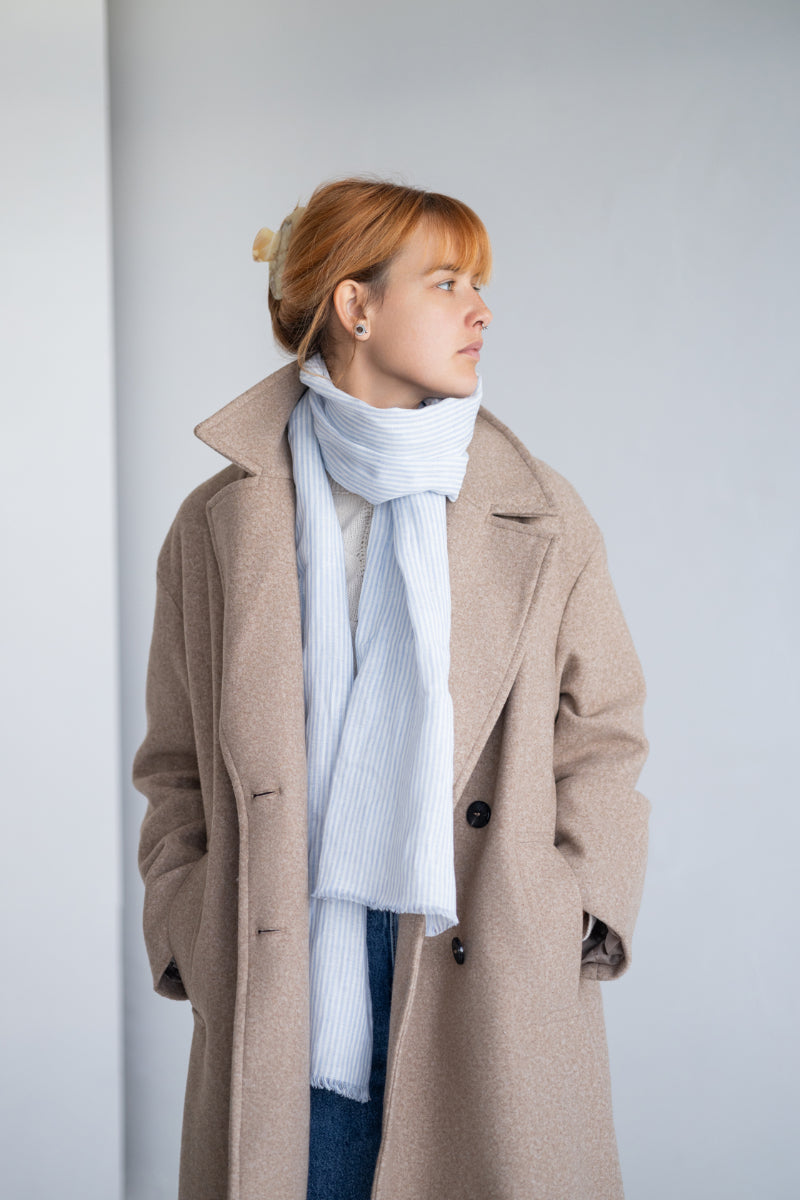 Woman wearing a striped linen scarf and white sweater against a plain background