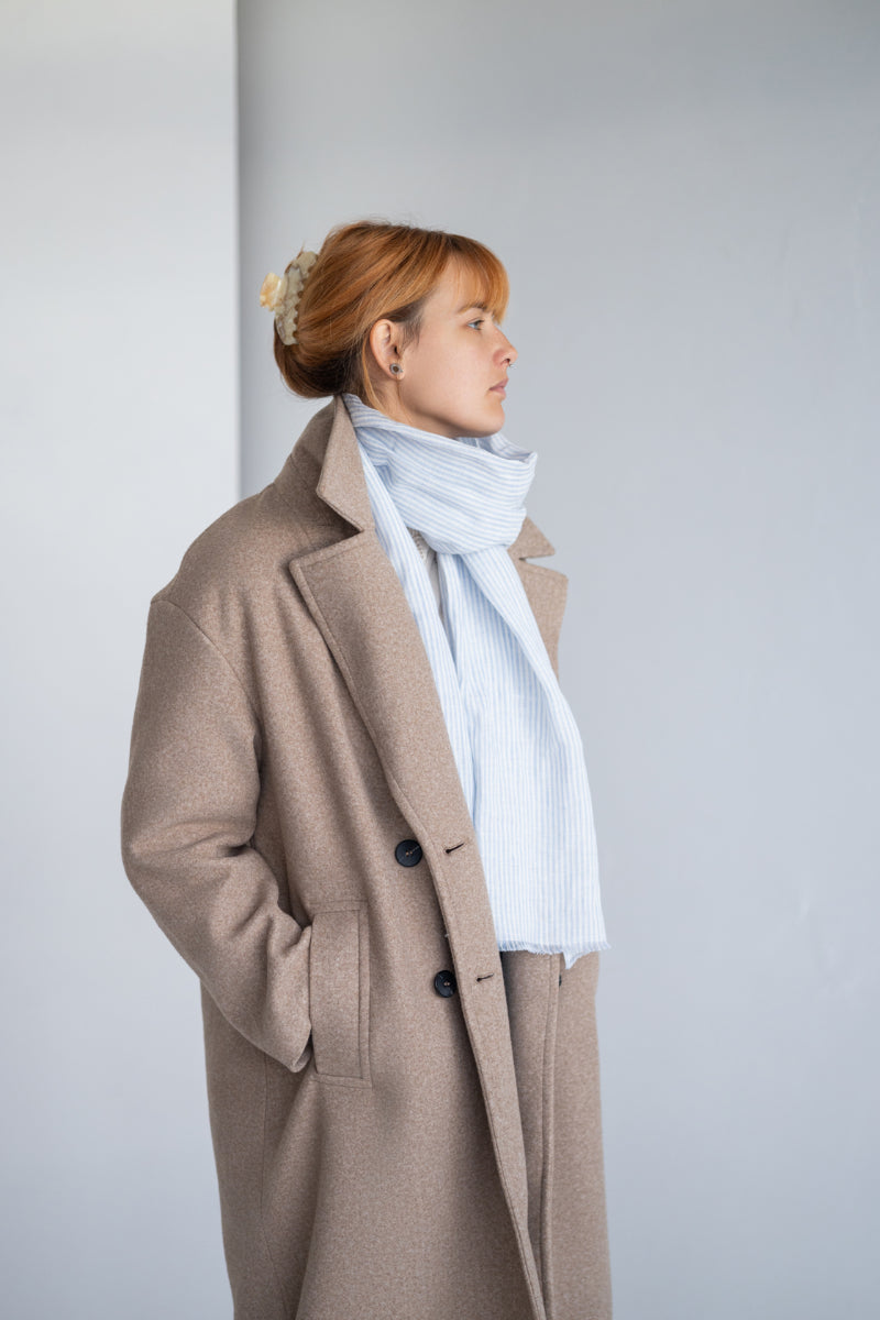 Woman wearing a striped linen scarf and white sweater against a plain background